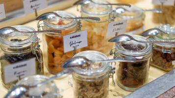 Una presentación de diversos alimentos en frascos de vidrio con tapas metálicas y cucharas, cada uno identificado con el tipo de alimento y la marca.