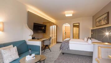 A hotel room with a sofa, a small table, a bed, a desk, and a TV.