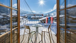 A balcony with a view of a snowy mountain landscape, a table, and two chairs. -  Hotel Sonne 4 Sterne Superior (Kirchberg in Tirol)