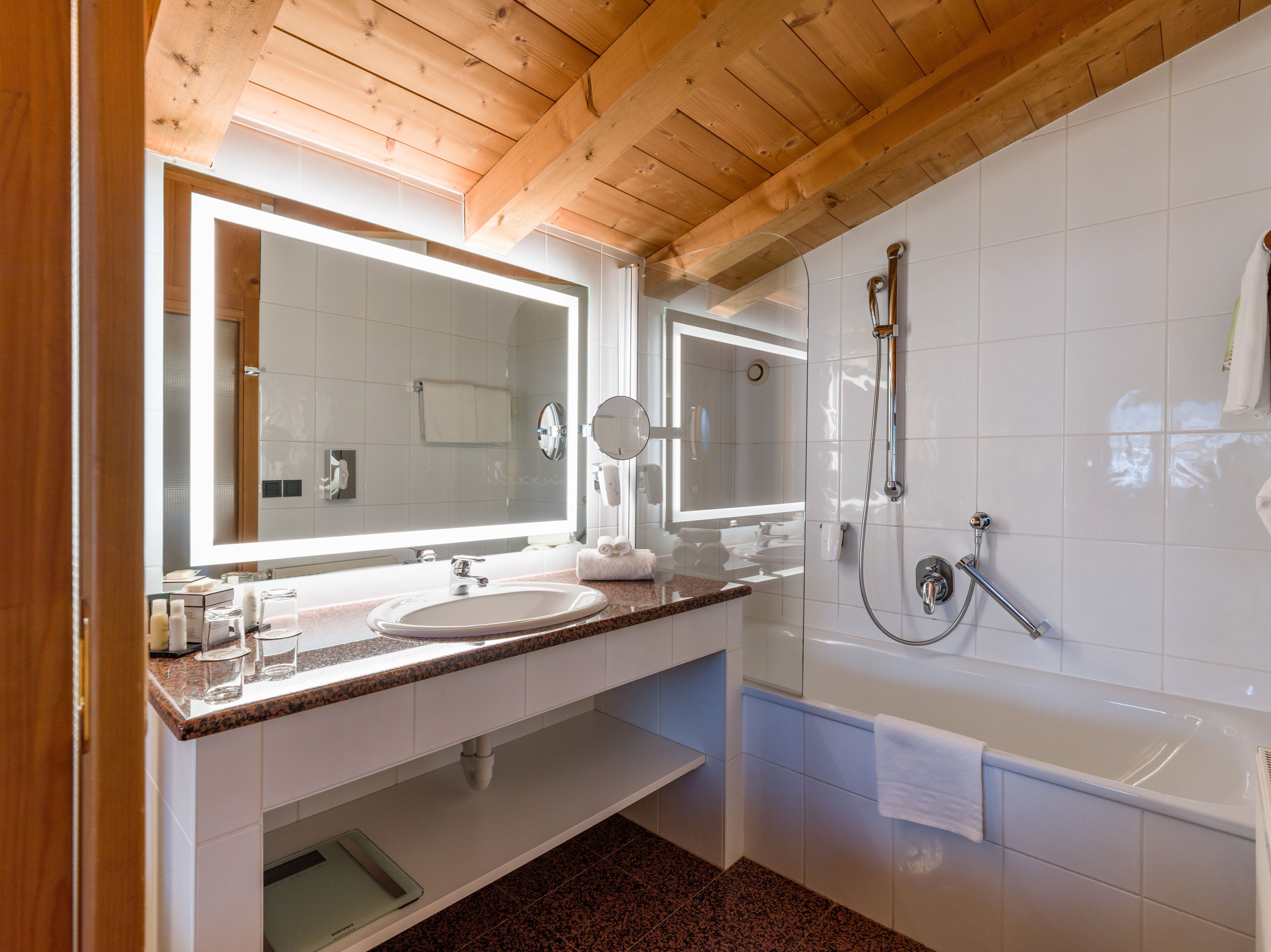A modern bathroom with a wooden ceiling, a large mirror, a sink, and a bathtub.