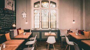 A cozy restaurant with wooden tables and chairs, a large window with stained glass, and a chalkboard menu on the wall. - Hotel Villa Klemm - Wiesbaden City (Wiesbaden)