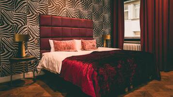 Un dormitorio con una pared estampada con diseño de cebra, un cabecero acolchado, una colcha roja y dos lámparas de noche.