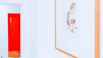 Un espacio galería minimalista con una obra enmarcada en la pared y una puerta roja al fondo.