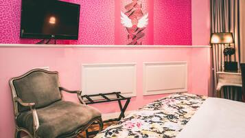 A bedroom with a pink leopard print wall, a bed with a floral bedspread, a vintage chair, a TV, and a radiator.