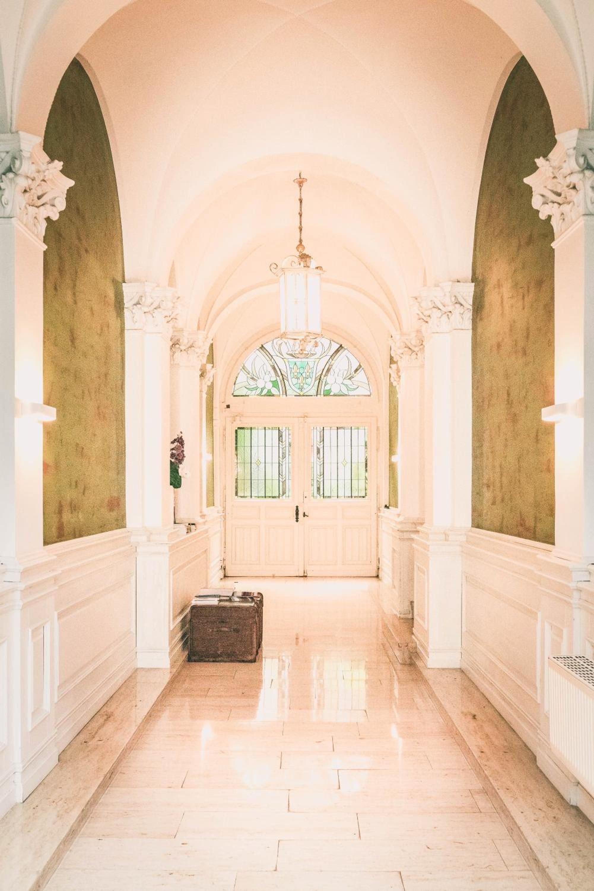 A hallway with a double door, a chandelier, and a suitcase on the floor.