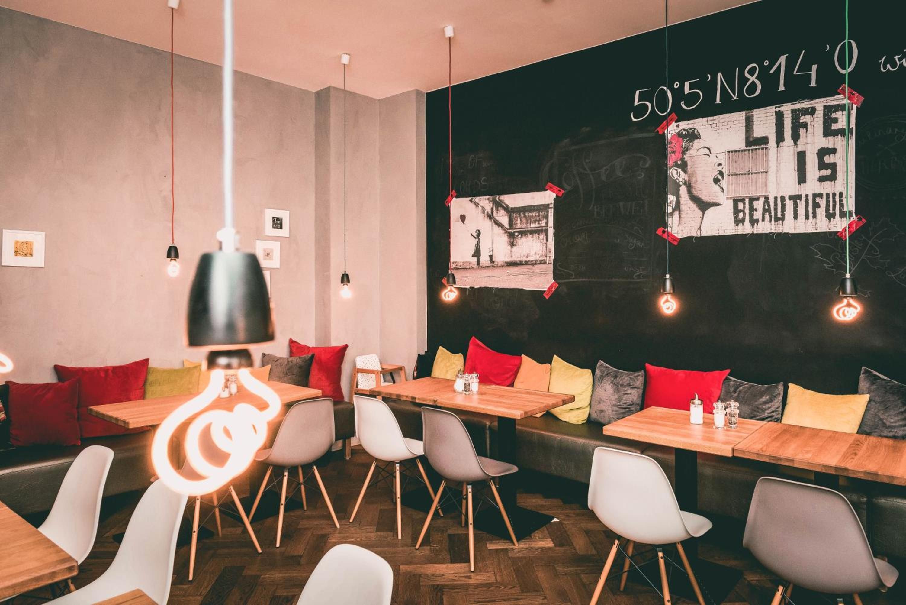 A restaurant interior with wooden tables, white chairs, and a blackboard with graffiti art.