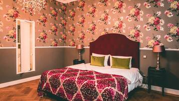 A bedroom with a floral wallpaper, a red headboard, and a patterned bedspread.