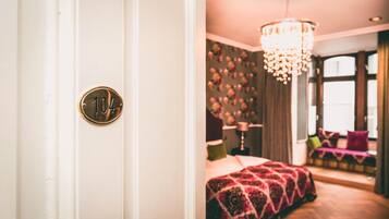 A hotel room with a bed, a chandelier, and a door with a number plate.