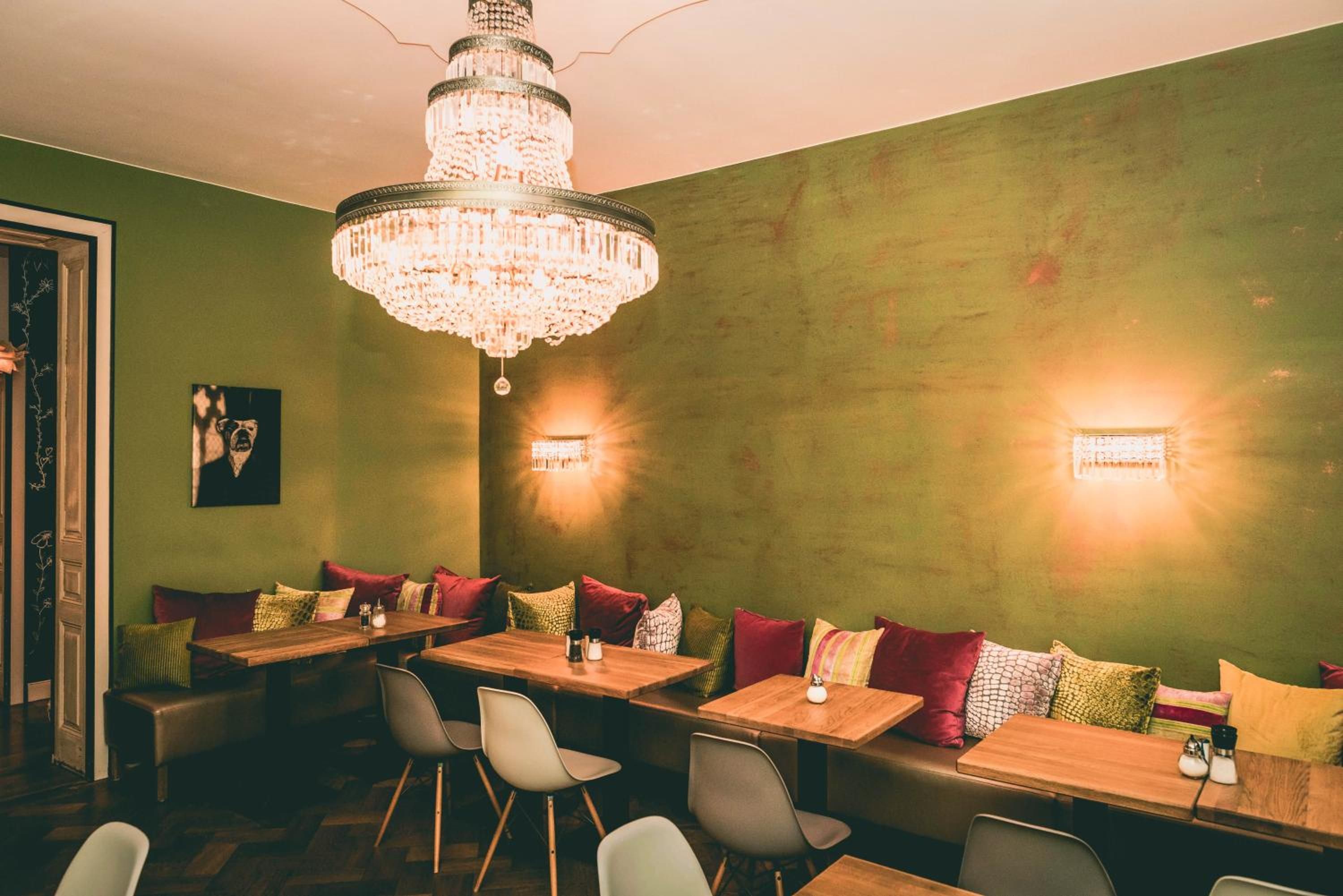 A restaurant interior with a chandelier, green walls, and multiple seating arrangements including booths and tables.