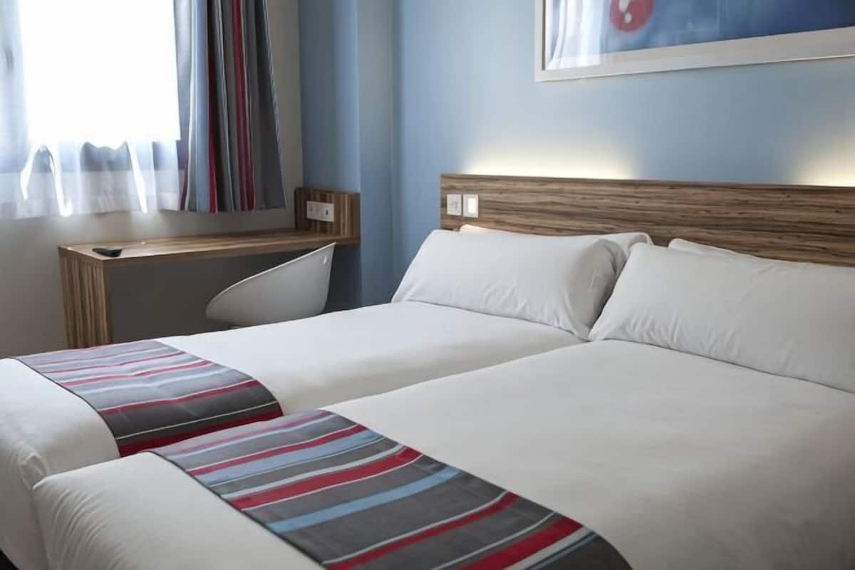 Una habitación de hotel con dos camas, un escritorio y una ventana con cortinas.