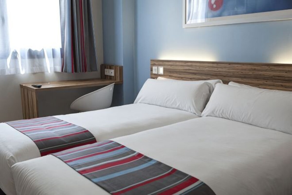 Ett hotellrum med två sängar, ett skrivbord och ett fönster med gardiner.