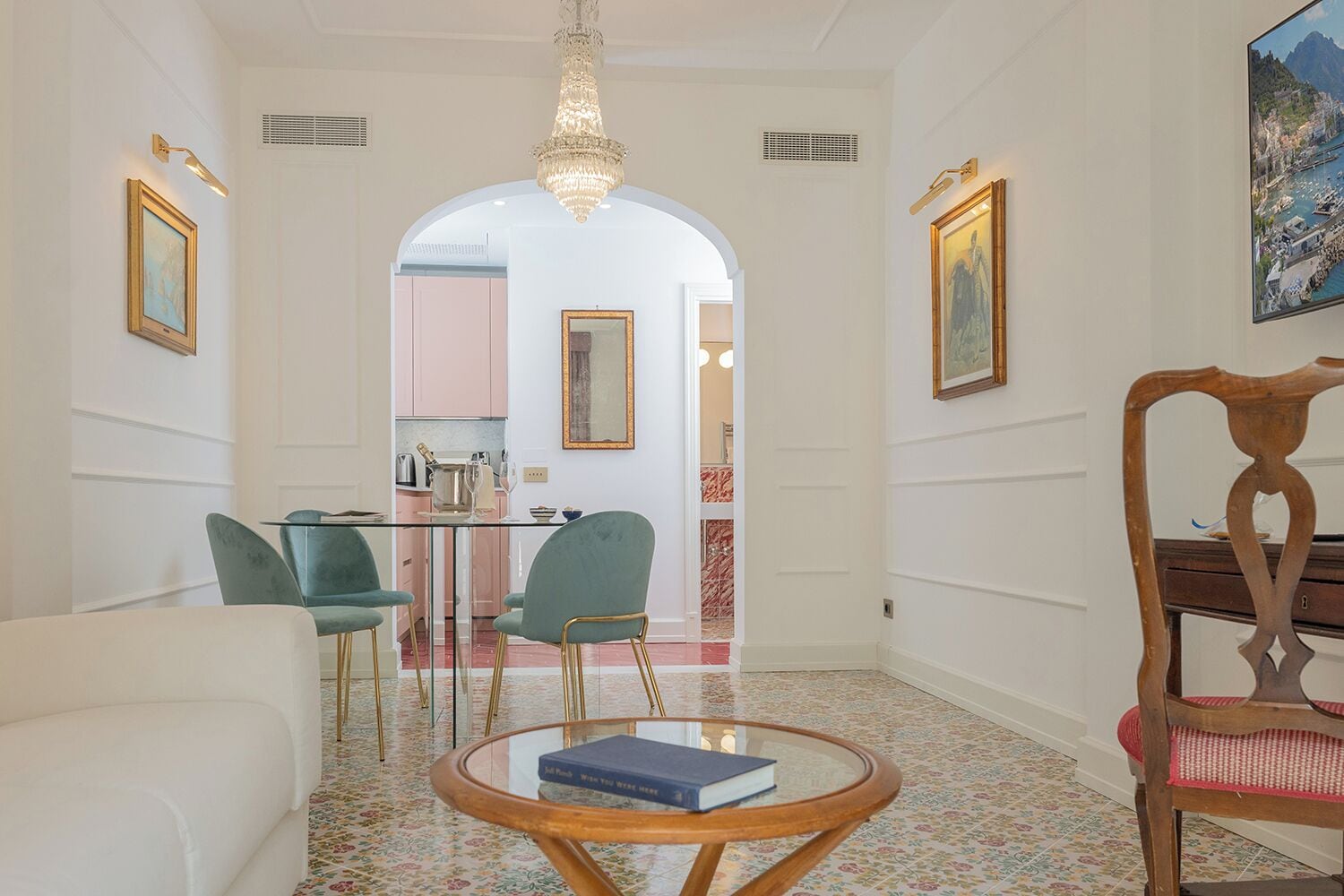 A spacious living room with a glass coffee table, a sofa, and a wooden chair. An archway leads to a kitchen area.