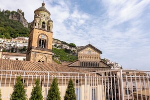 Un edificio histórico con una torre de campanas y una estructura más pequeña, rodeado de viviendas y una colina.