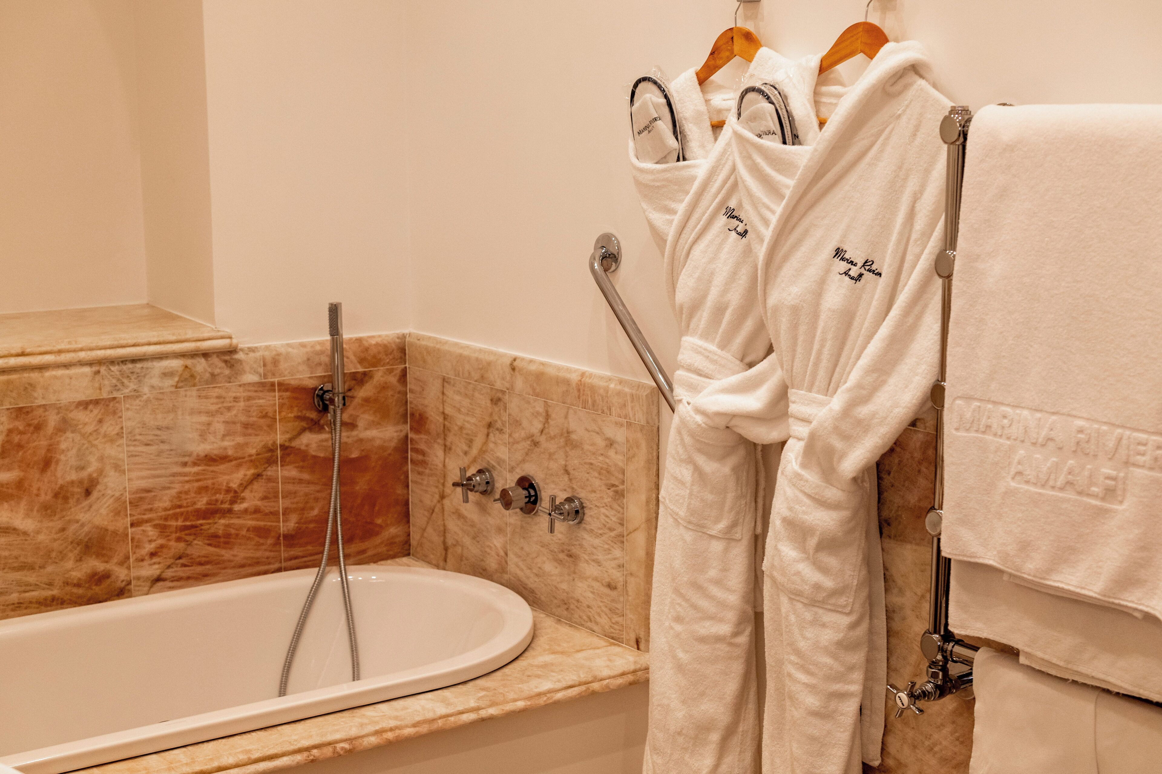 A bathroom with a marble sink, a bathtub, and a towel rack with robes.