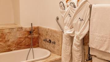 A bathroom with a marble sink, a bathtub, and a towel rack with robes.