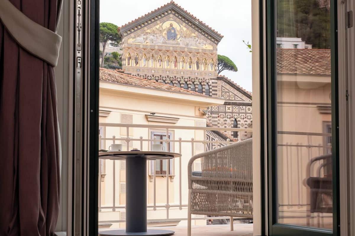 A room with a view of a historic building with a cross on top, a tiled floor, and a sliding glass door.