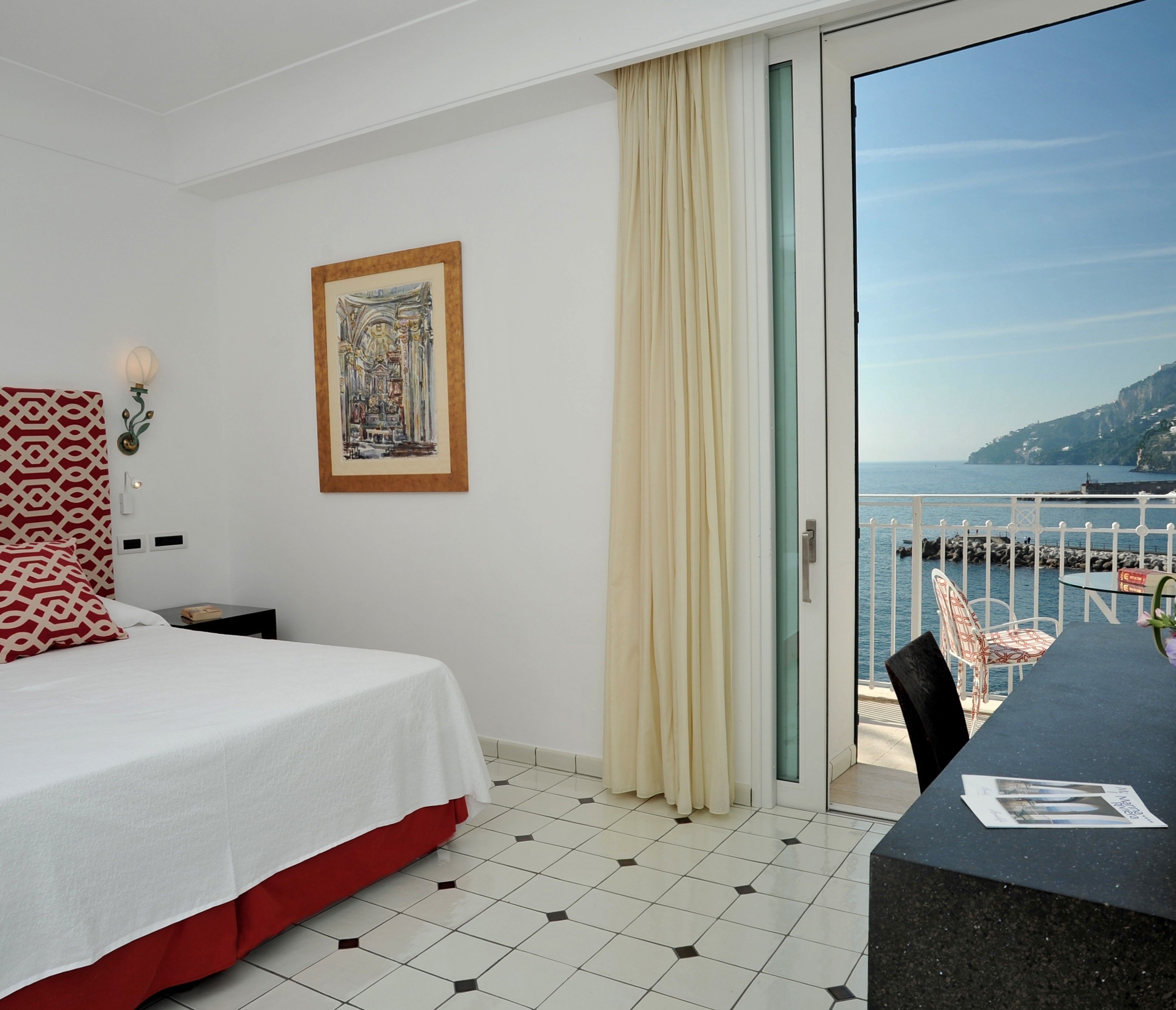 Una habitación de hotel con cama, una mesa de comedor, vistas al mar y un cuadro en la pared.