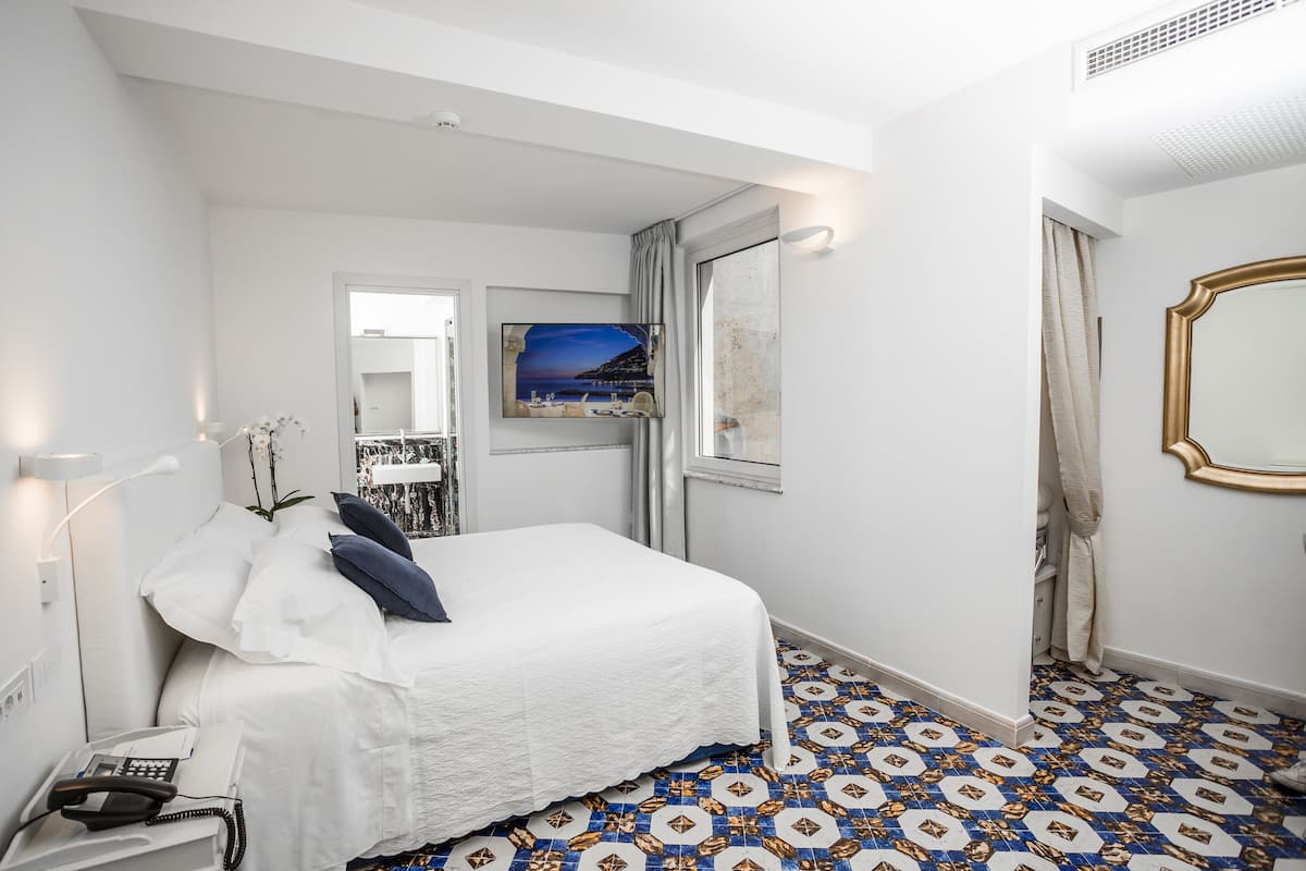 A hotel room with a bed, a telephone, a painting, and a patterned floor.