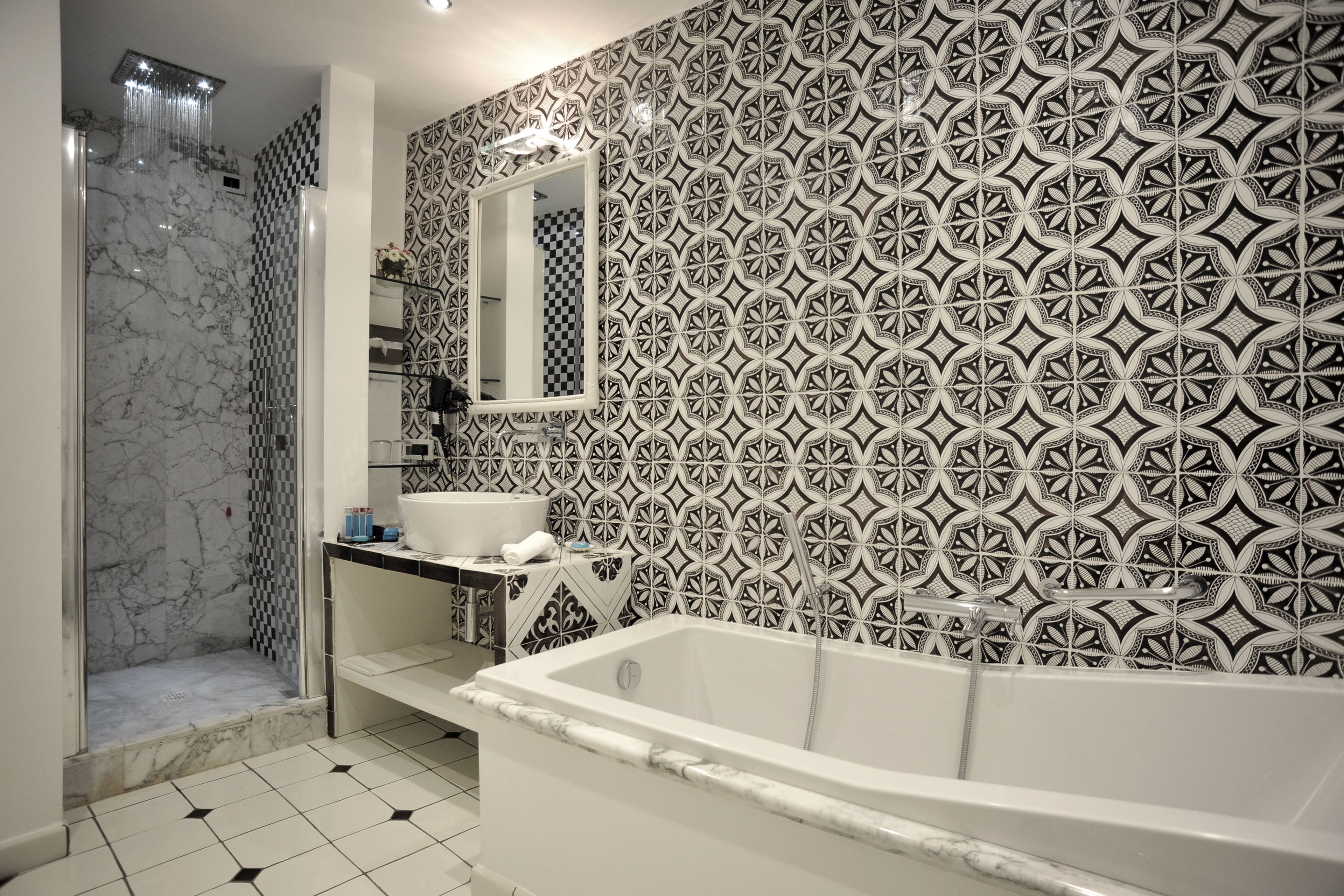 A bathroom with a marble shower, a bathtub, and a sink with a patterned backsplash.