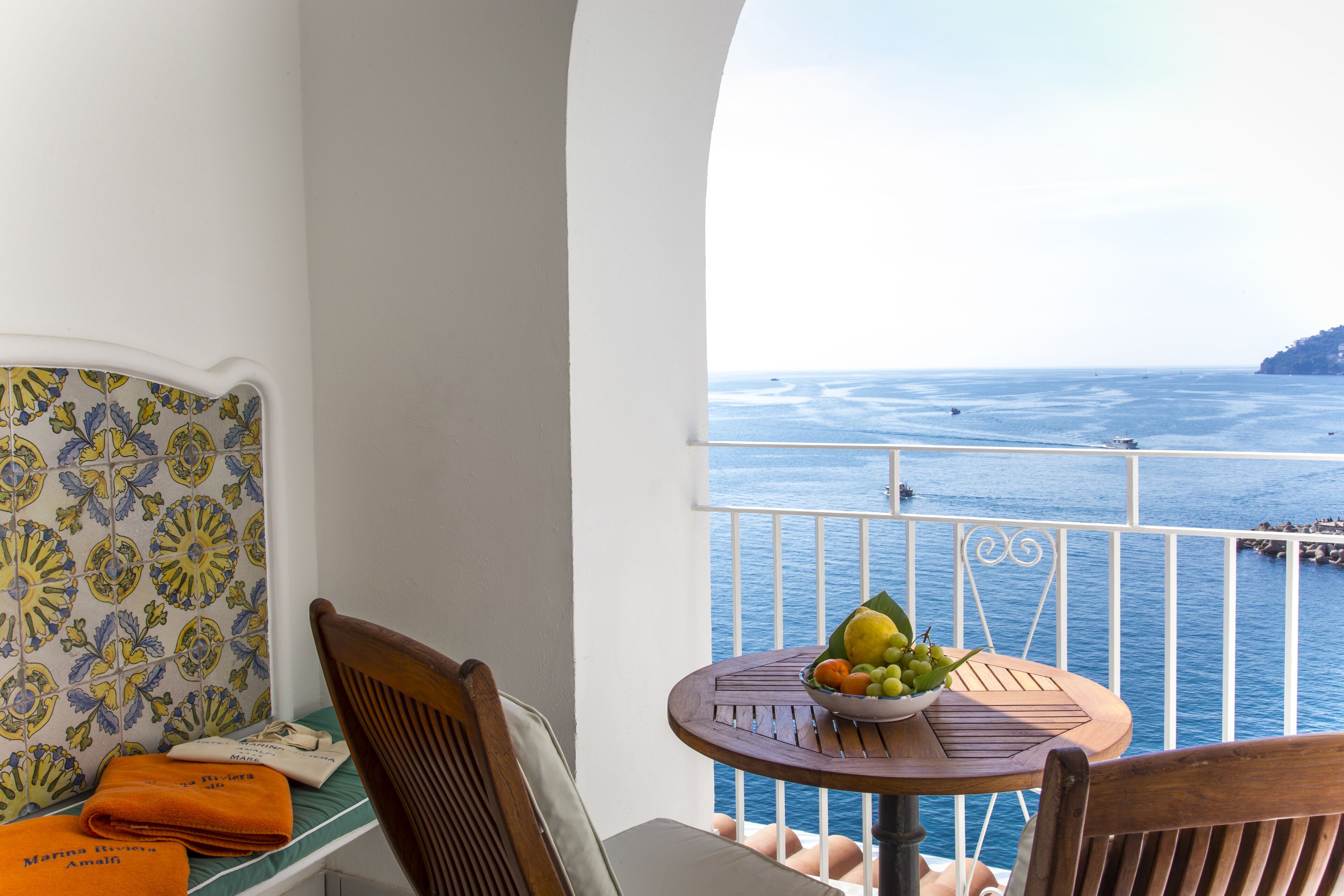 Een balkon met uitzicht op zee, een ronde houten tafel met een schaal fruit en een stoel.