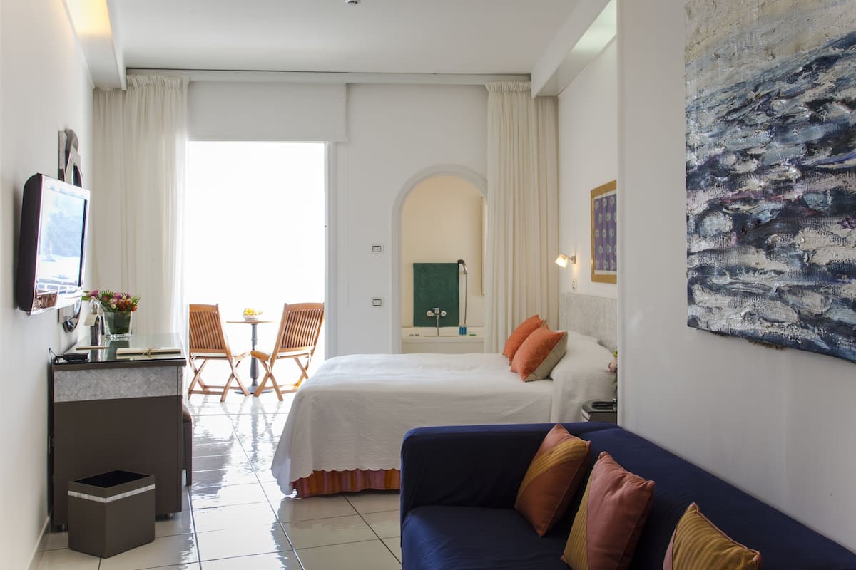 A hotel room with a bed, a sofa, a desk, a chair, and a painting on the wall.