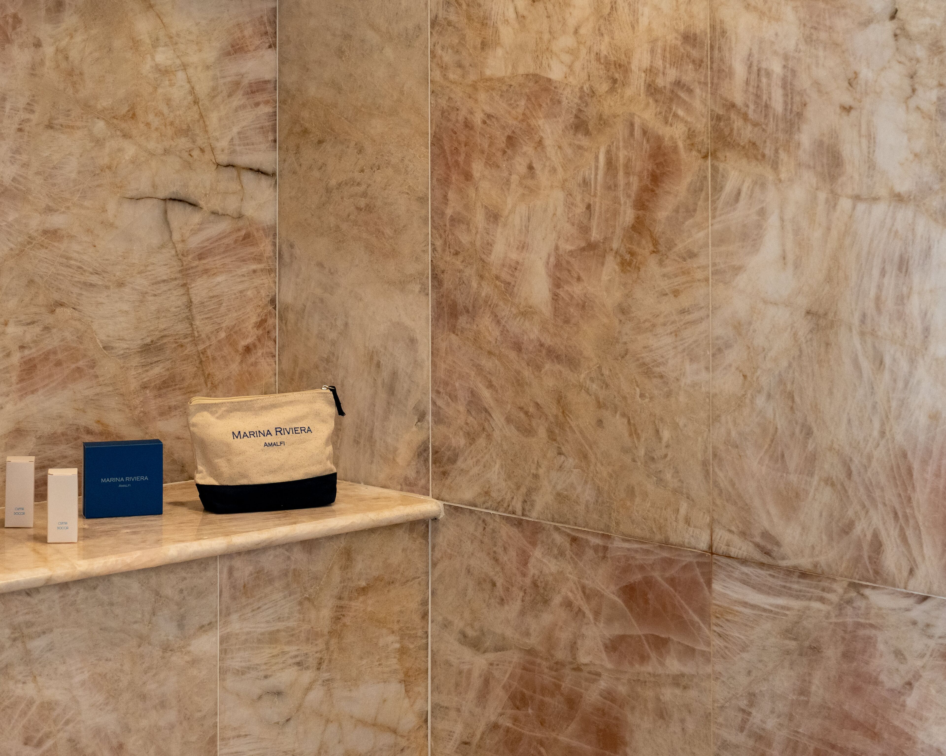 Ein Badezimmer mit Marmorwänden, einer Ablage mit einer Tasche mit dem Aufdruck "MARINA RIVIERA" und zwei Kartons.
