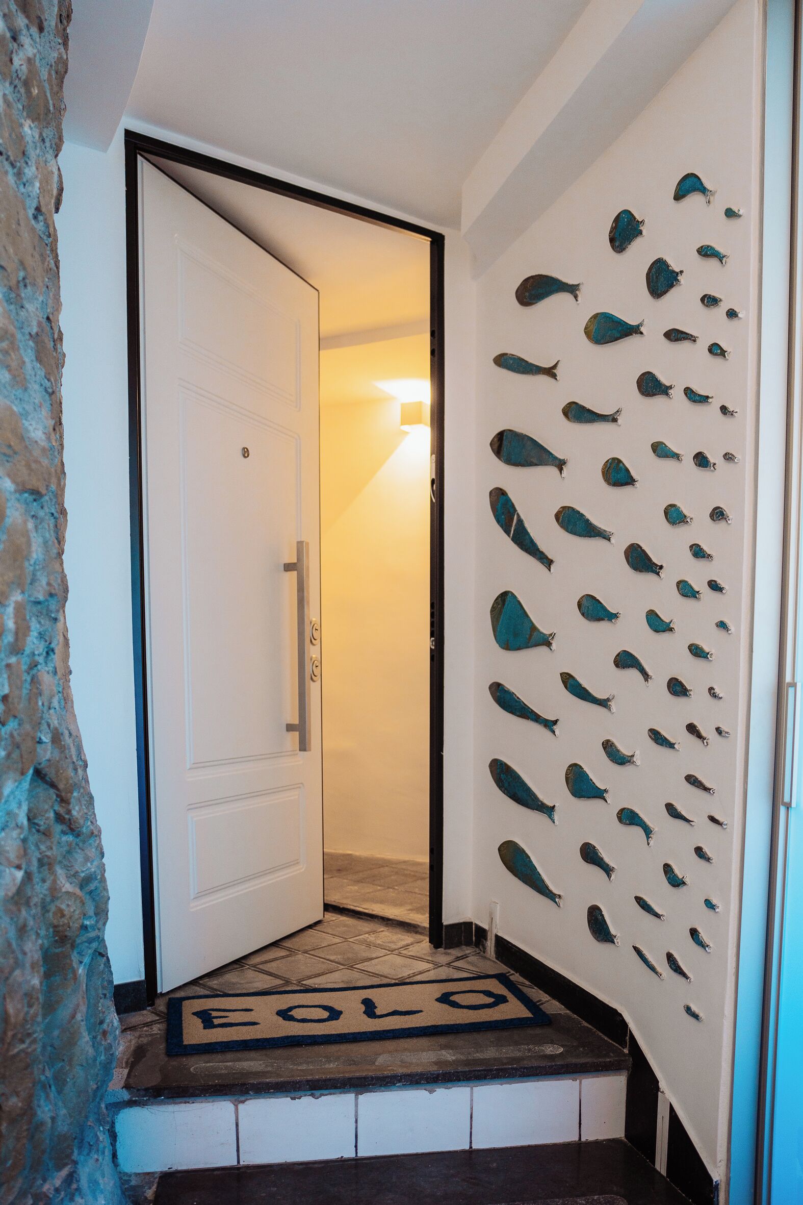 A hallway with a white door, a fish-themed wall decoration, and a doormat with the word "FOLLO".