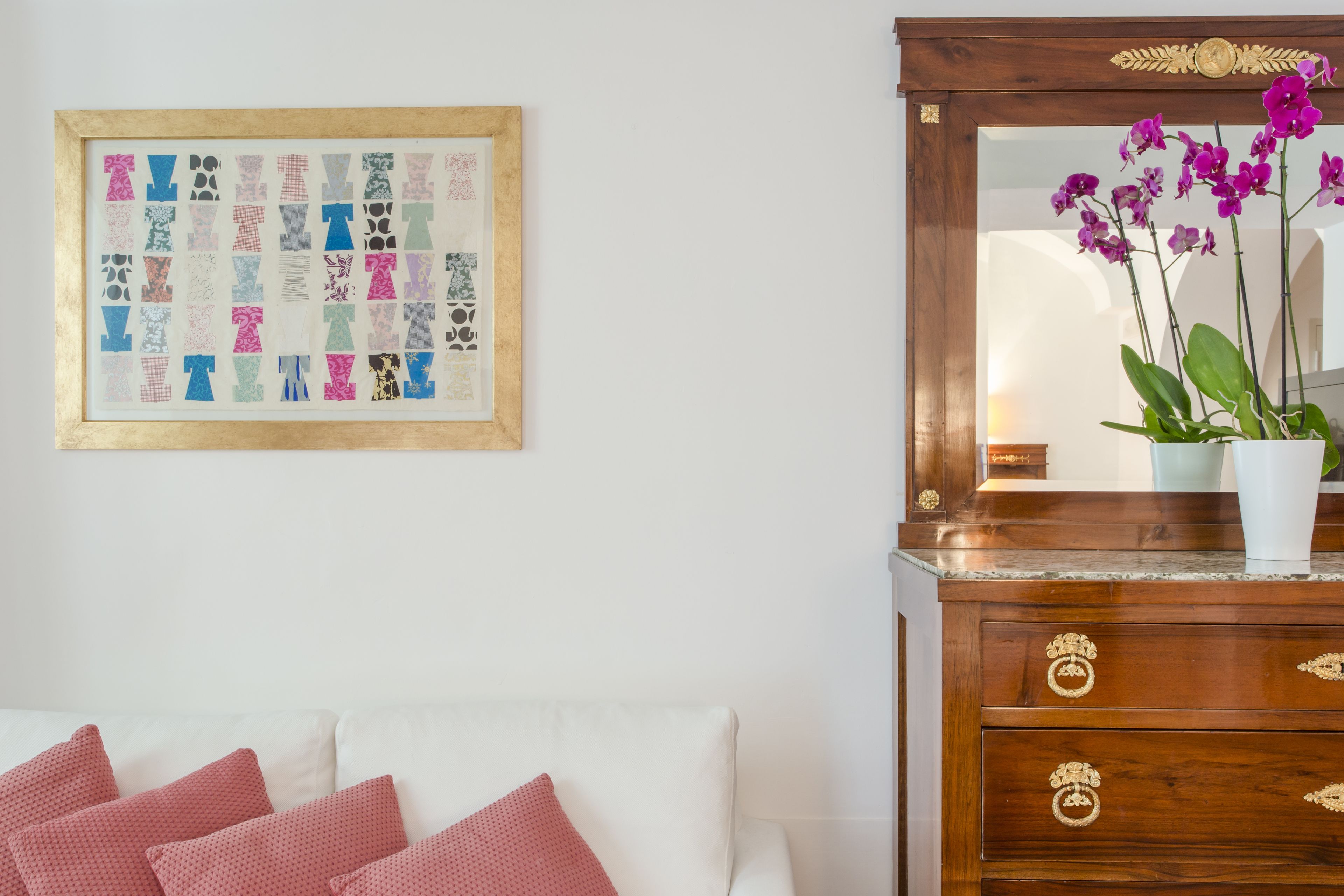 Une pièce avec un canapé blanc, une commode en bois dotée d’un miroir et un collage encadré accroché au mur.