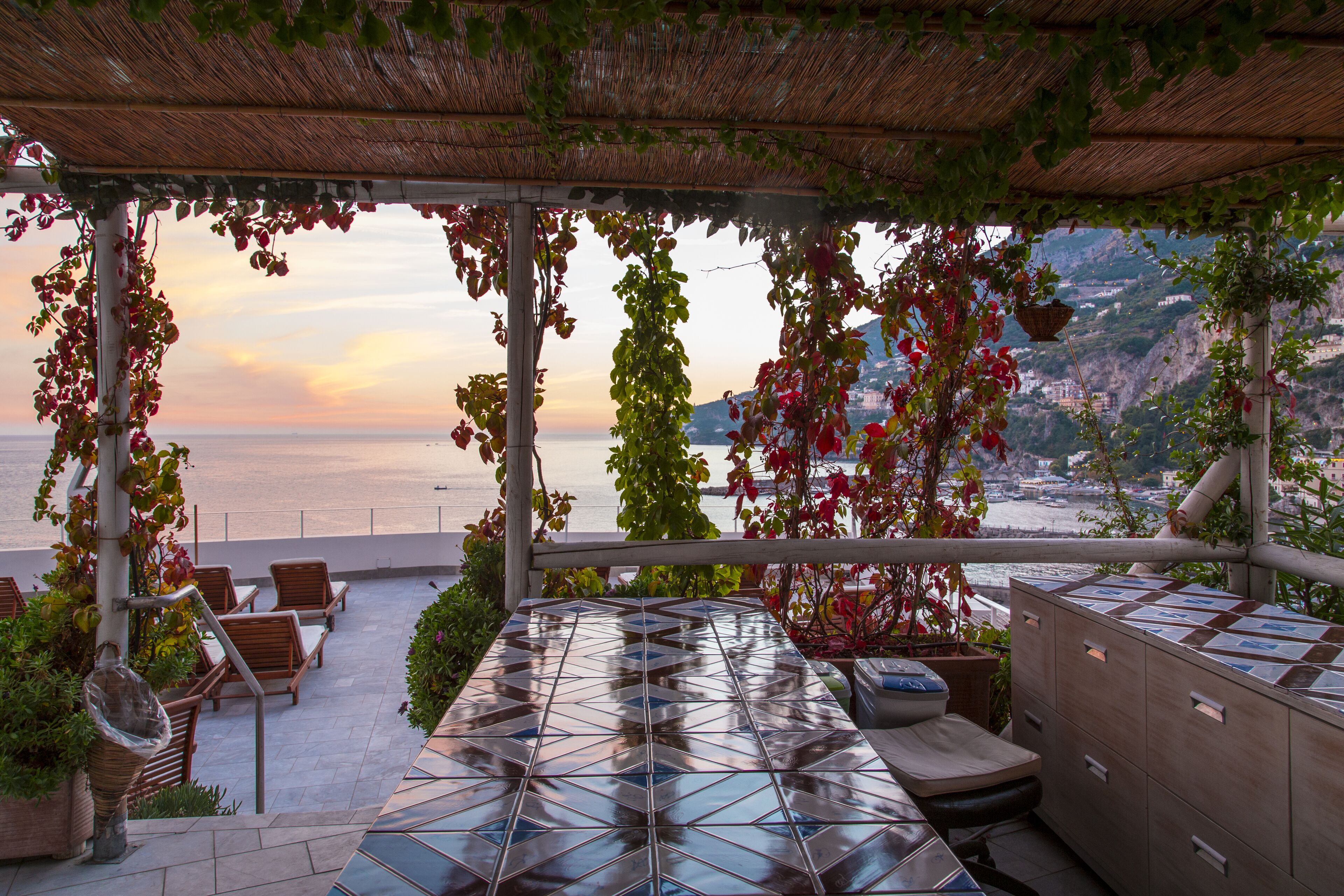 Una terrazza con vista sul mare, arredi in legno e piante in vaso.