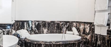 A bathroom with a marble tub, a sink, and a tiled floor.