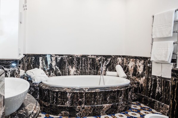 A bathroom with a marble tub, a sink, and a tiled floor.