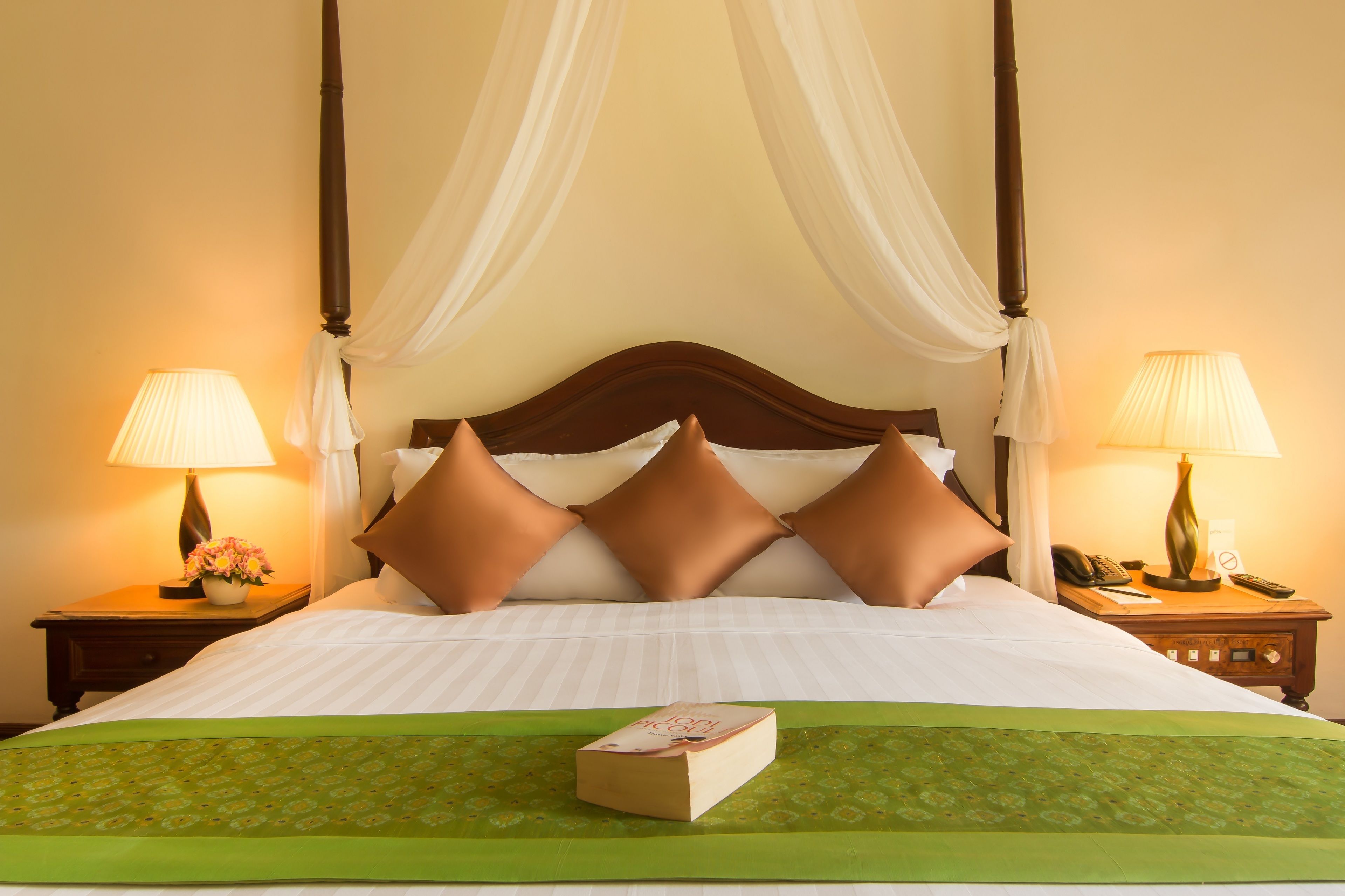 A four-poster bed with white linens, two bedside lamps, and a green bed runner.