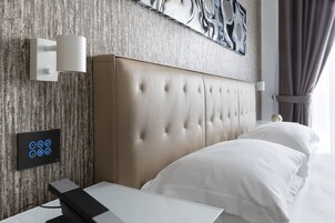 Een moderne hotelkamer met een gestapeld hoofdeinde, een nachtkastje, een bedieningspaneel aan de muur en een groot abstract kunstwerk boven het bed.
