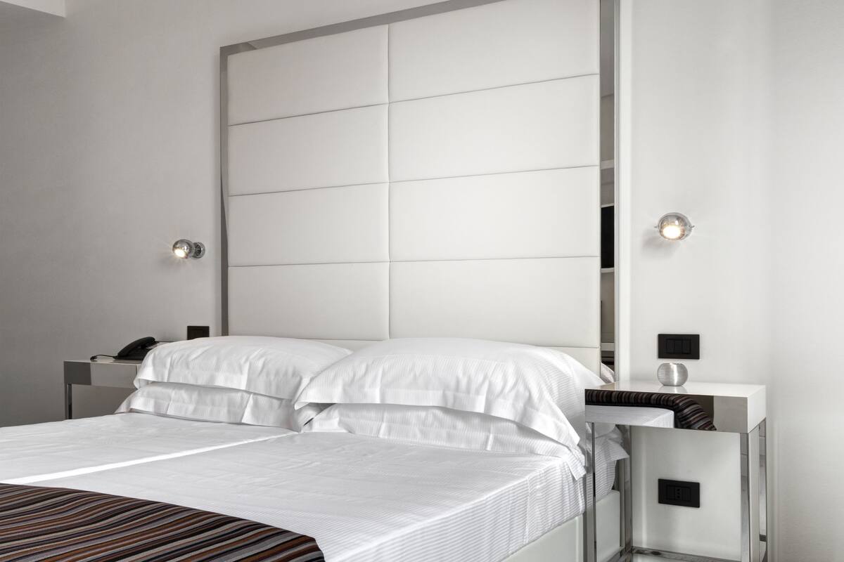 Une chambre d’hôtel moderne avec un grand lit, deux tables de chevet et une tête de lit dotée d’un panneau lumineux.