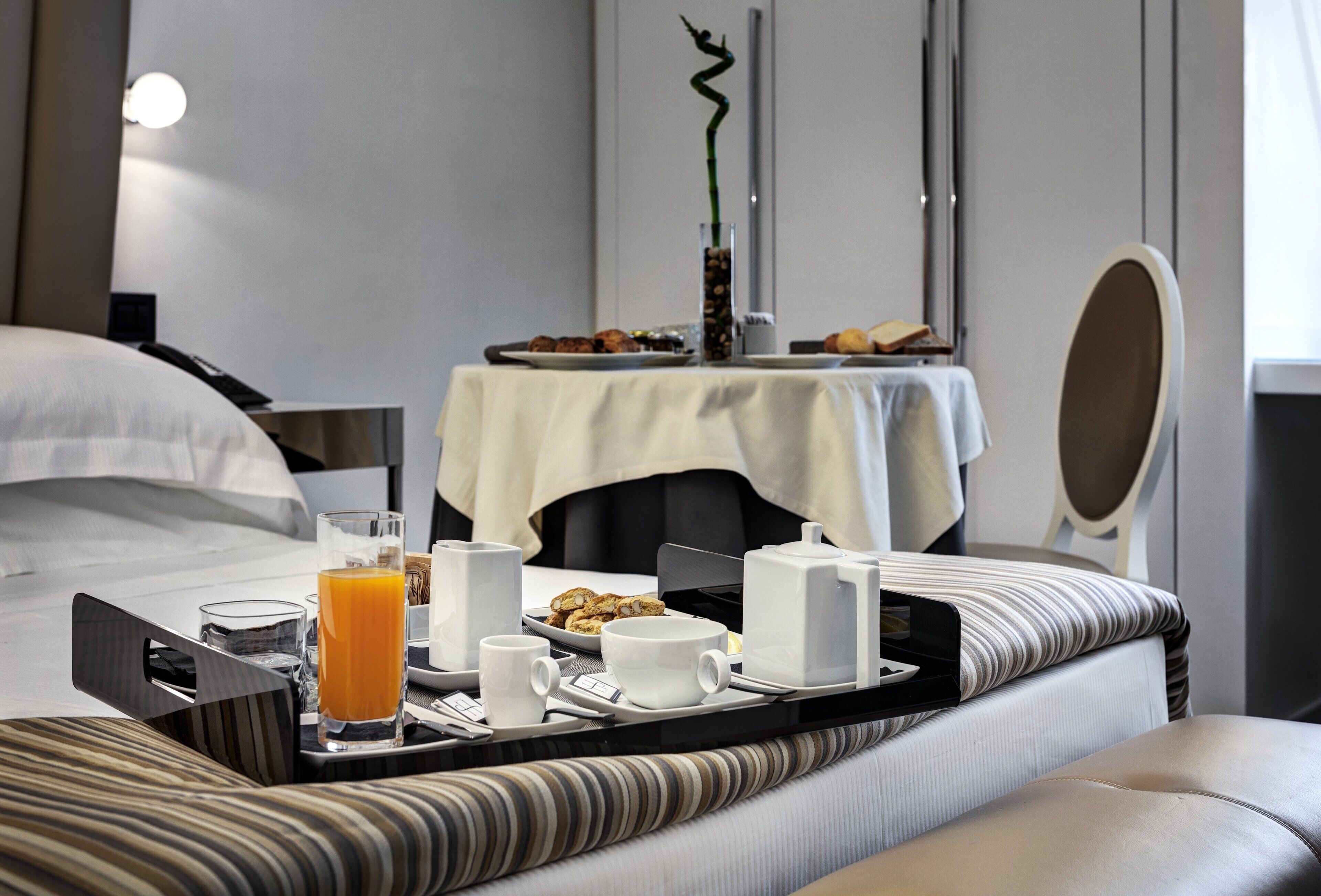 Una camera d'albergo con un vassoio per la colazione ordinato sul letto, un comodino con un vaso e uno specchio.