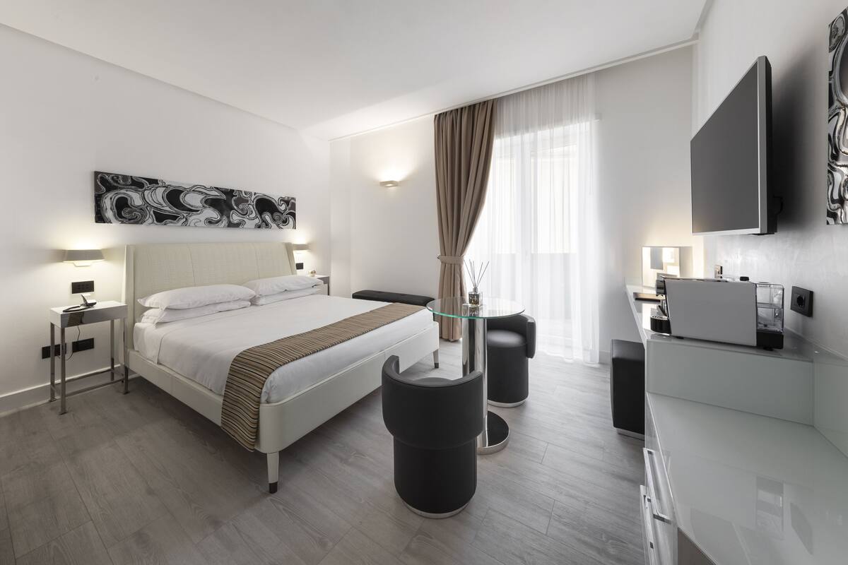 Une chambre d’hôtel moderne dotée d’un grand lit, de tables de chevet, d’une table basse en verre, d’un bureau et d’un téléviseur à écran plat.