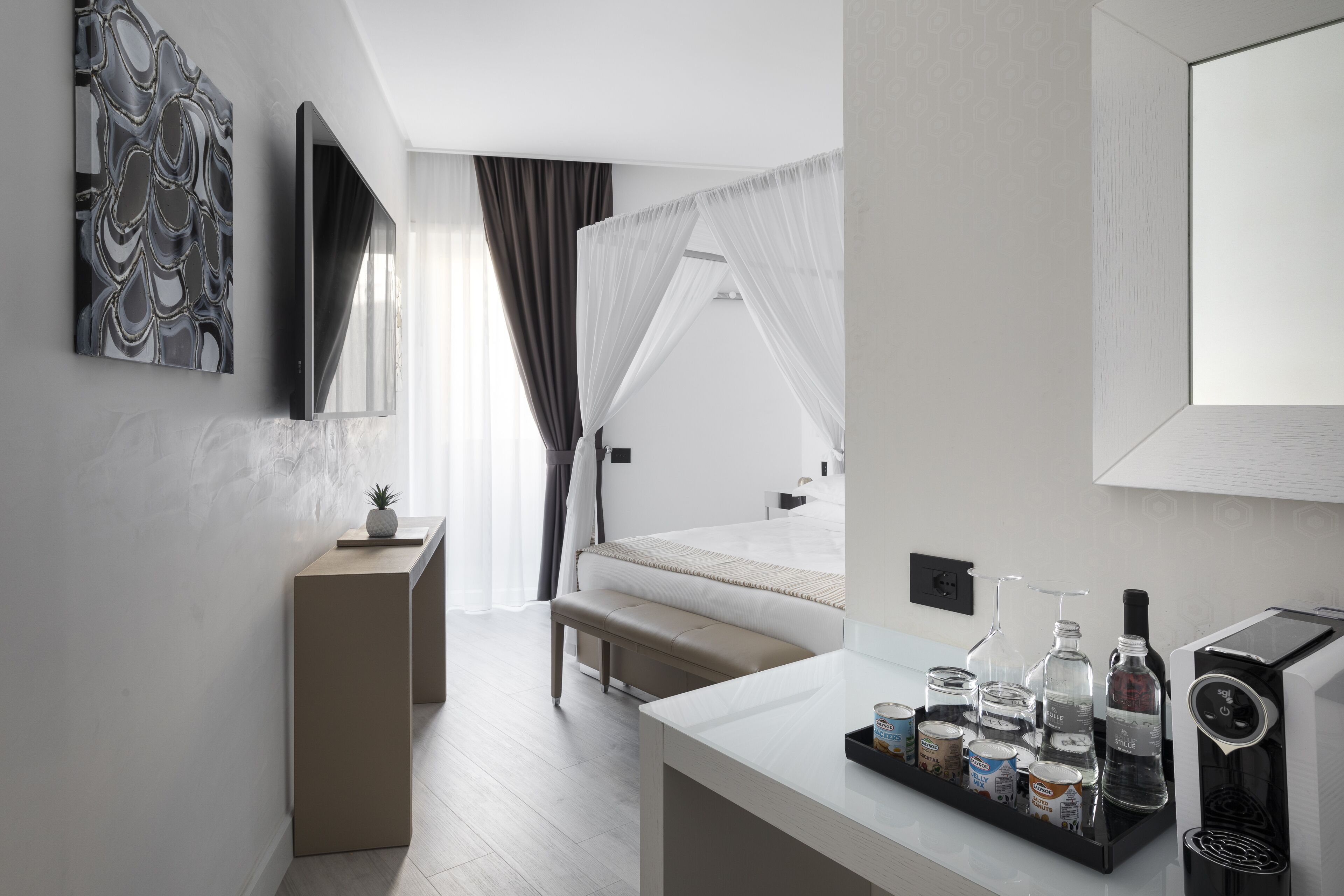 Una habitación de hotel moderna con cama, mesita de noche y una bandeja con bebidas y aperitivos.