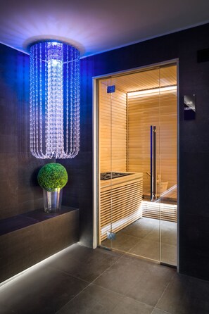 A modern interior with a glass door leading to a sauna area, a decorative light fixture, and a small green plant. - LHP Napoli Palace & spa (Naples)