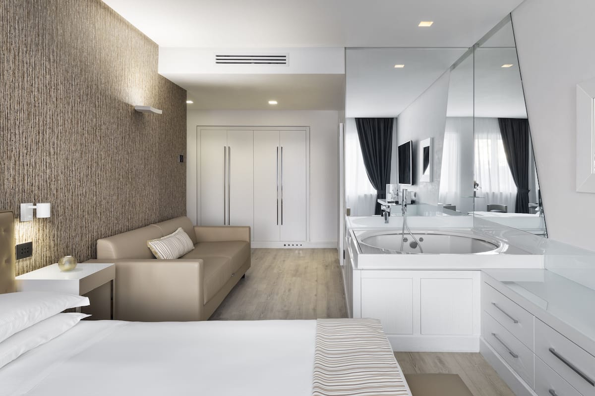 Une chambre d’hôtel moderne dotée d’un grand lit, d’un canapé, d’une coiffeuse avec un miroir et d’un mur décoratif en bois.
