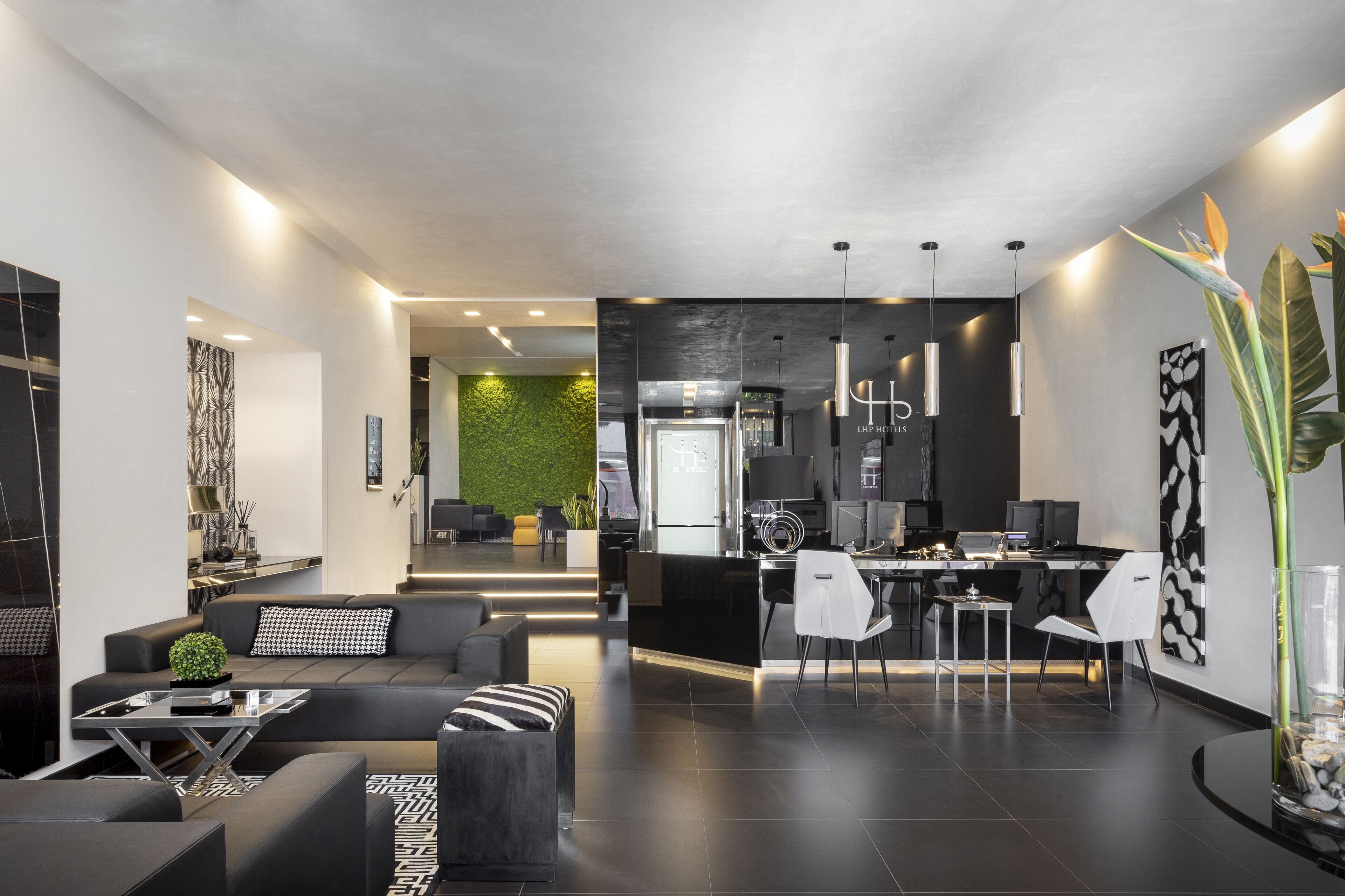 Een moderne hotellobby in zwart-wit kleurenschema, met een zithoek, een receptiebalie en een groene wand.