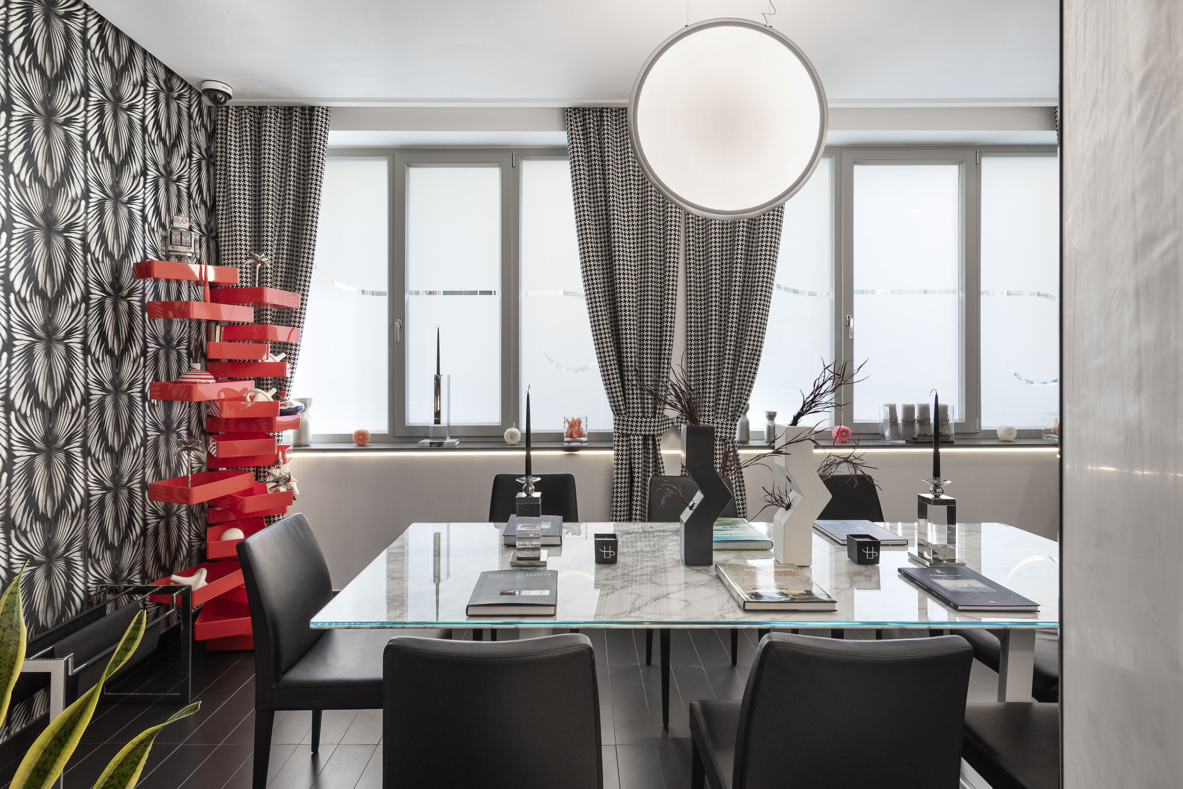 Et moderne spiseområde med et glasbord, sorte stole og en rød dekorativ genstand.
