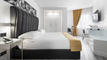 Una habitación de hotel moderna con una cama grande, un escritorio con silla, un televisor y un armario.