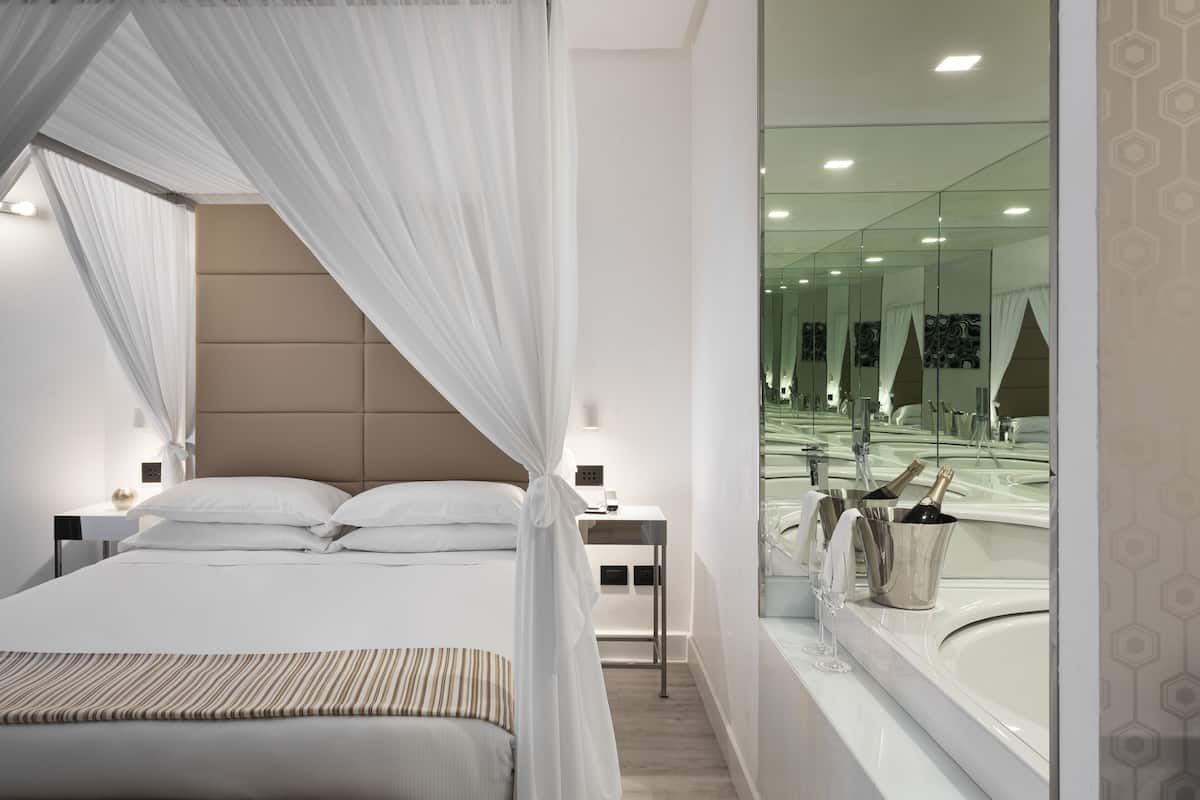Une chambre d’hôtel moderne avec un grand lit, une table de chevet, une commode, un miroir et une vue sur la salle de bain.