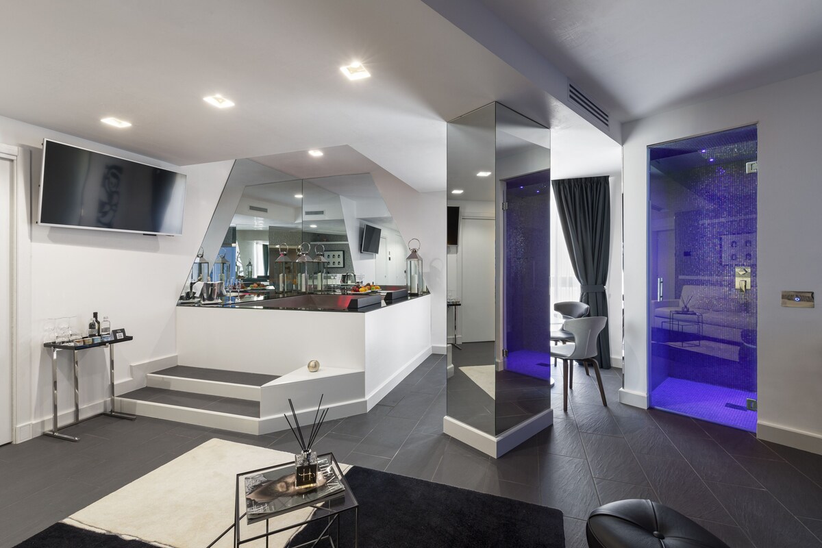Ein modernes Wohnzimmer mit Küchenbereich, einer Treppe und einem Badezimmer mit blauer Beleuchtung.