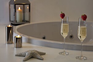 Una vasca da bagno con due bicchieri da champagne, ognuno decorato con una fragola, e una candela accesa su una superficie bianca.
