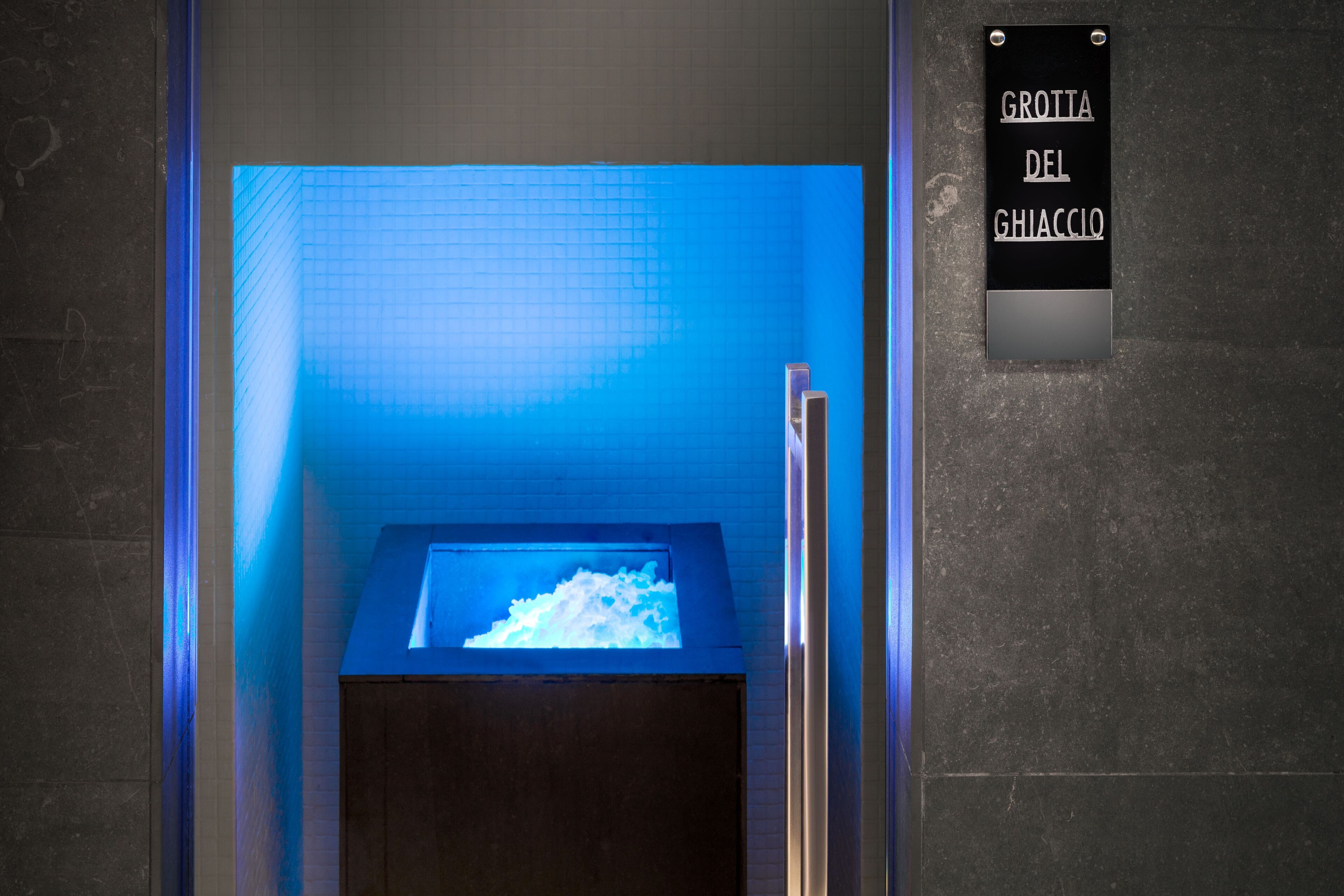 A bathroom with a blue-lit sink and a sign reading "Grotia del Ghiaccio".