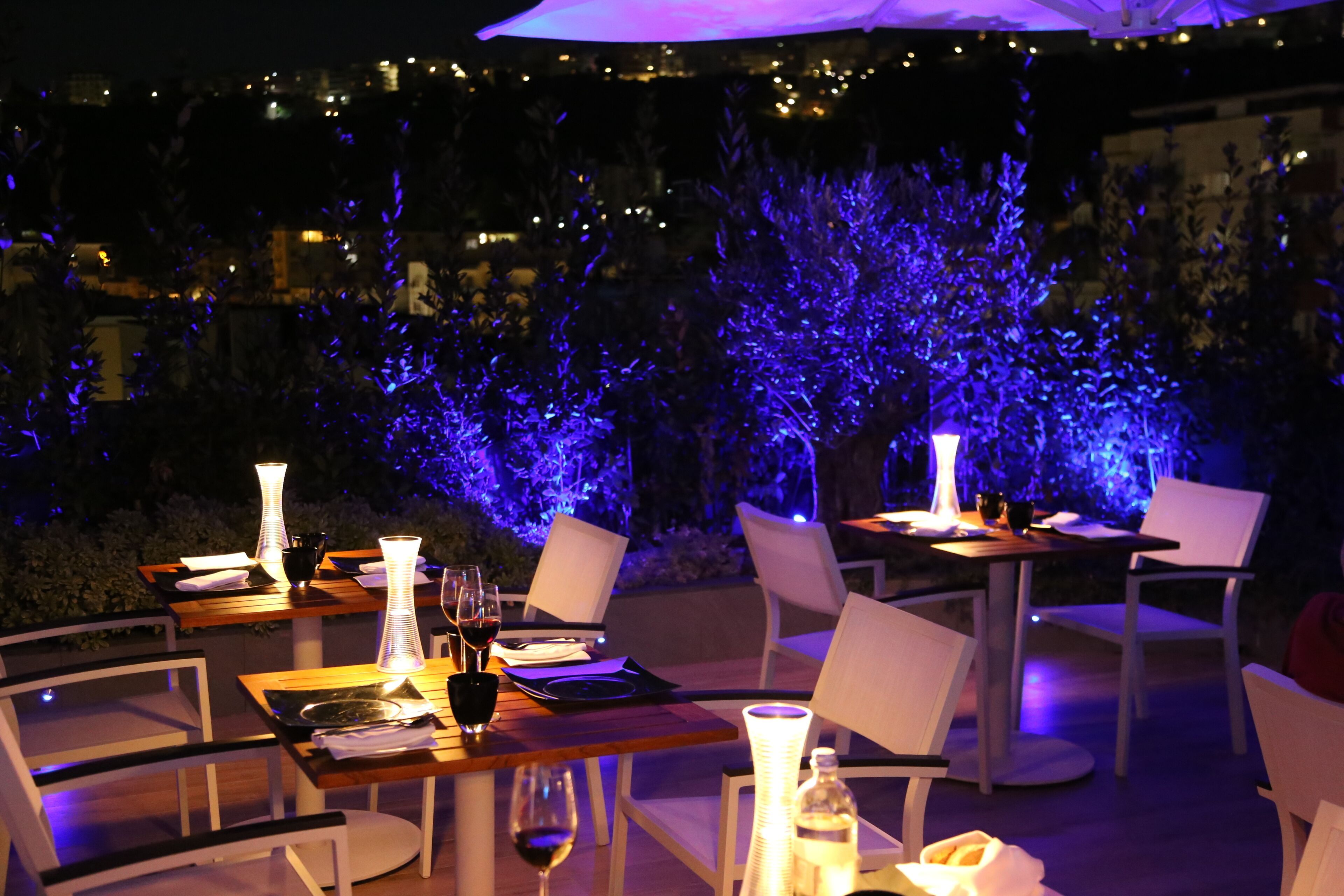 Un'area pranzo all'aperto con tavoli e sedie, illuminata da luci soffuse.