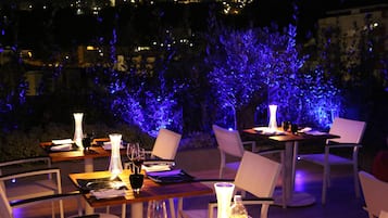 Un'area pranzo all'aperto con tavoli e sedie, illuminata da luci soffuse.