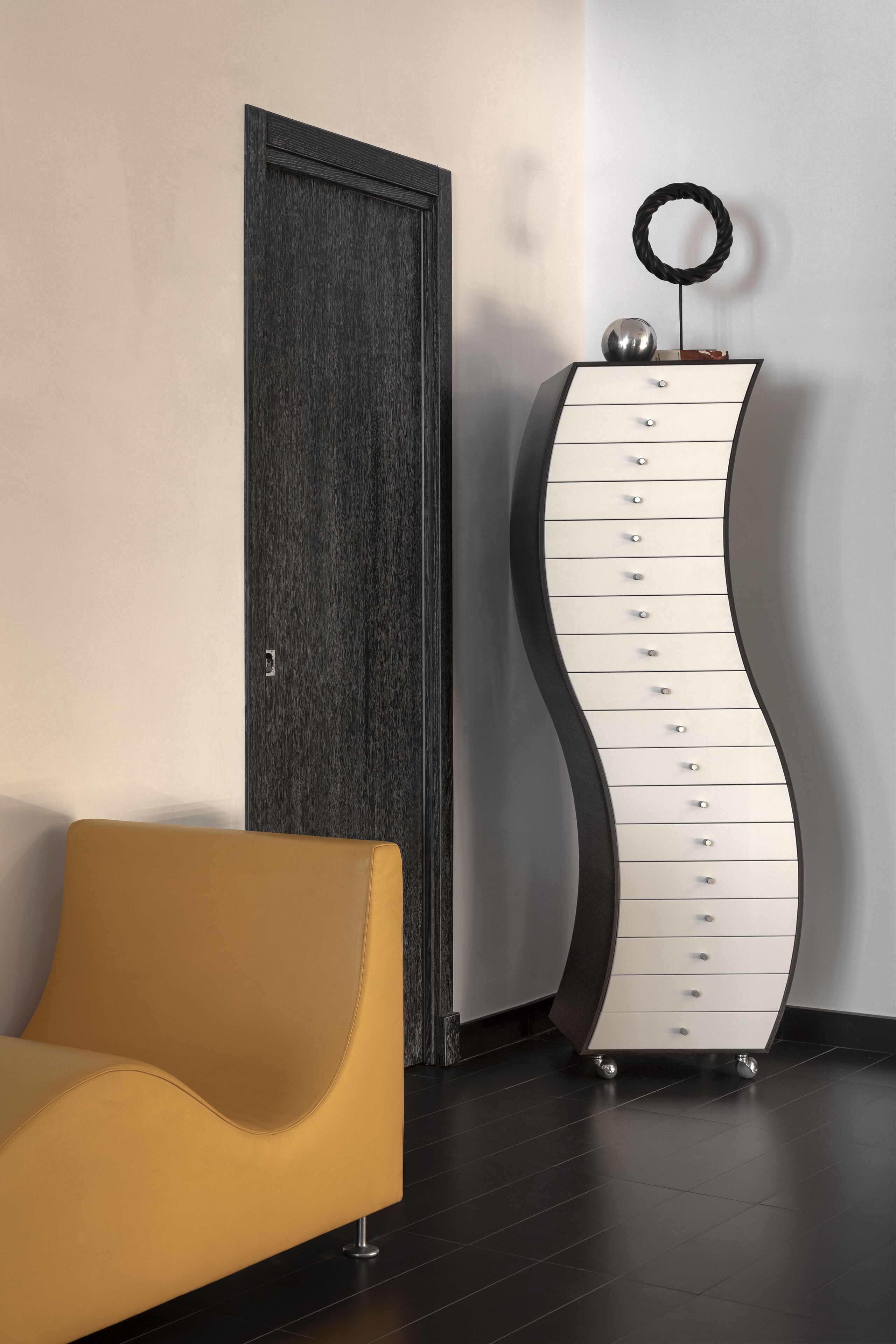 A modern room with a curved white dresser, a yellow chair, and a dark wooden door.