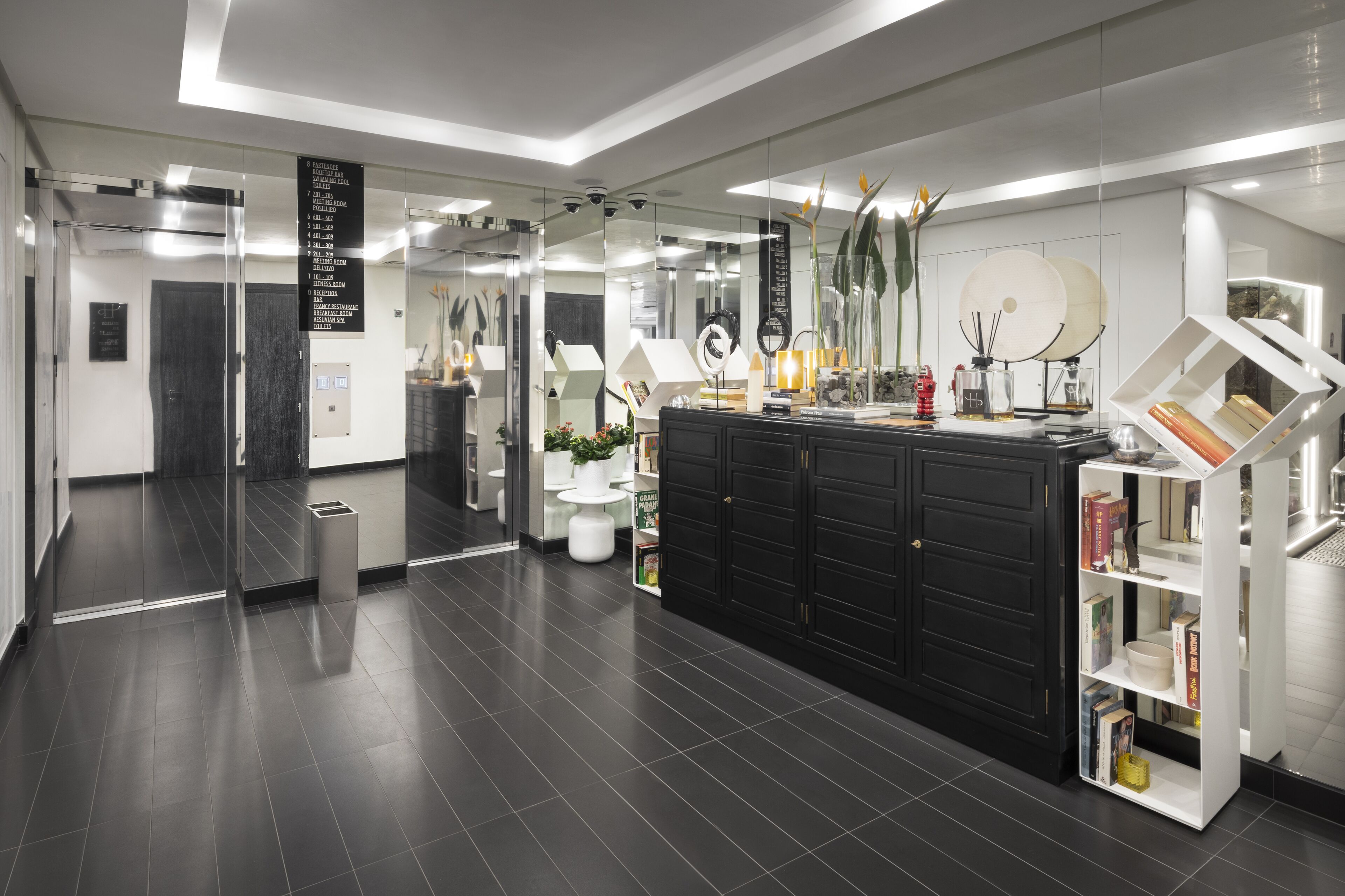 A modern bathroom with a black vanity, white shelves, and a glass partition.